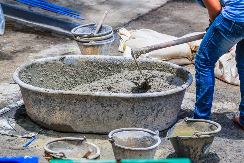 Pracovník míchá beton v kbelíku s písekem a vodou.