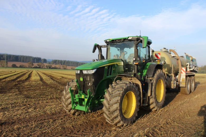 Zelený traktor s přívěsem na poli bez registrace