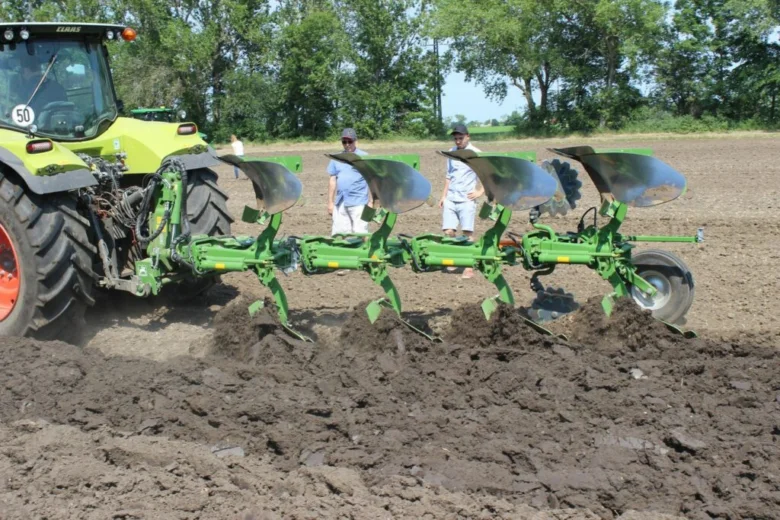 Zelený traktor s neseným pluhem obrání pole při sledování mužů.