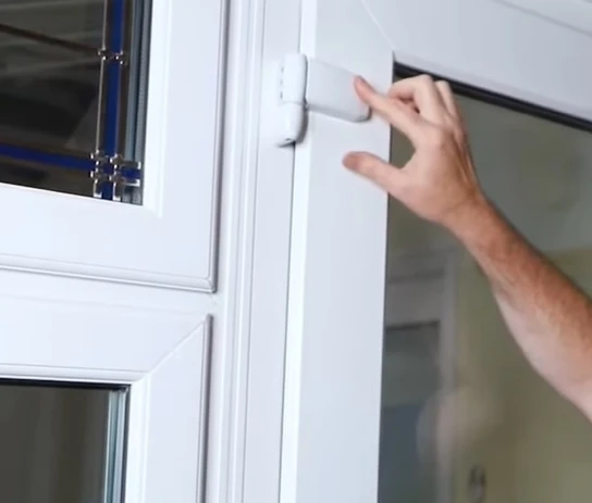 Ruka upravuje přítlak na plastových dveřích z PVC.