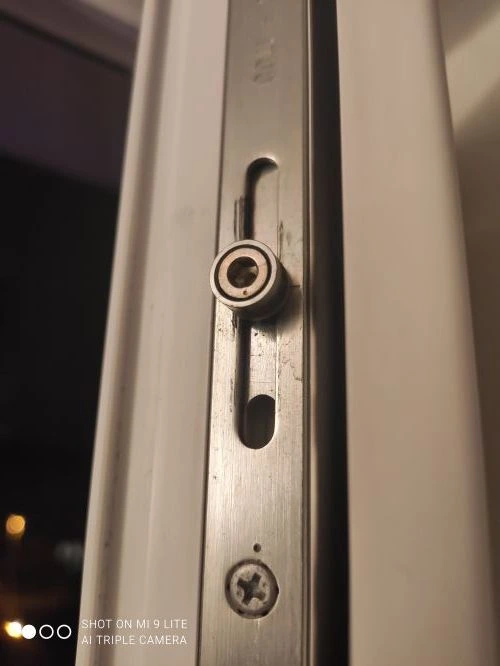 Detail plastového okna s kovovým zamkovým mechanismem.
