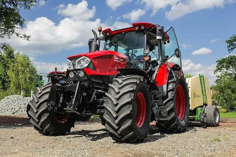 Červený traktor s přívěsem na štěrku.