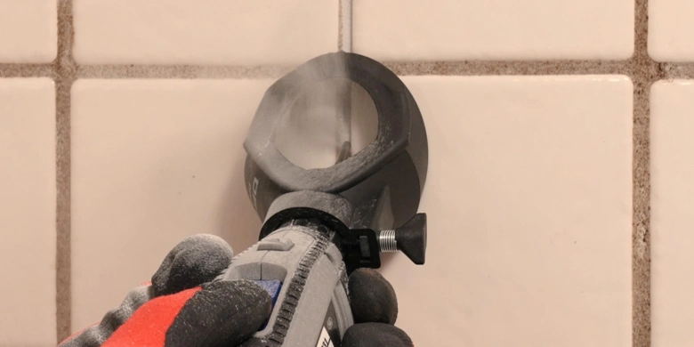Oscilátor odstraňuje starou spárovací hmotu z dlaždic na stěně.