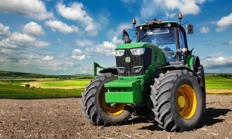 Zelený traktor na oraném poli pod modrou oblohou
