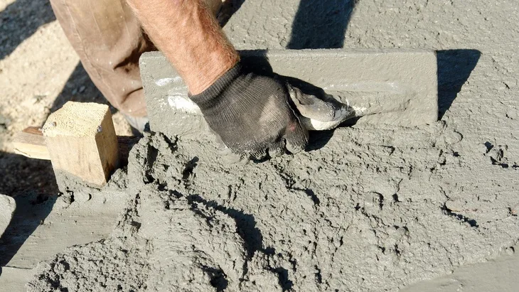 Stavebník hladí čerstvý beton na staveništi.