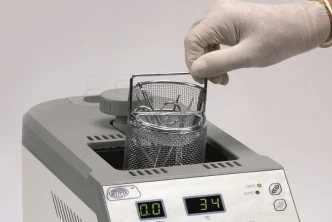 Ruce v rukavicích vkládají nástroje do autoklavu pro sterilizaci.