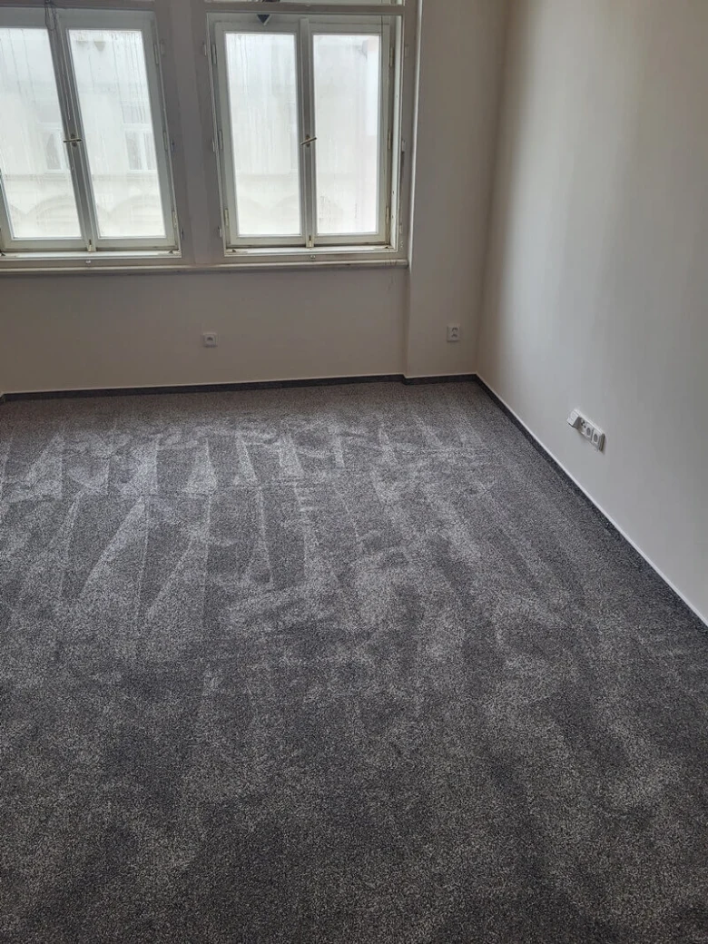 Uložený šedý koberec na betonové podlaze v prázdné místnosti.
