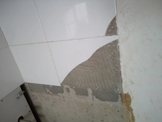Částečně odstraněné dlaždice odhalují lepidlo na sádrokartonu.
