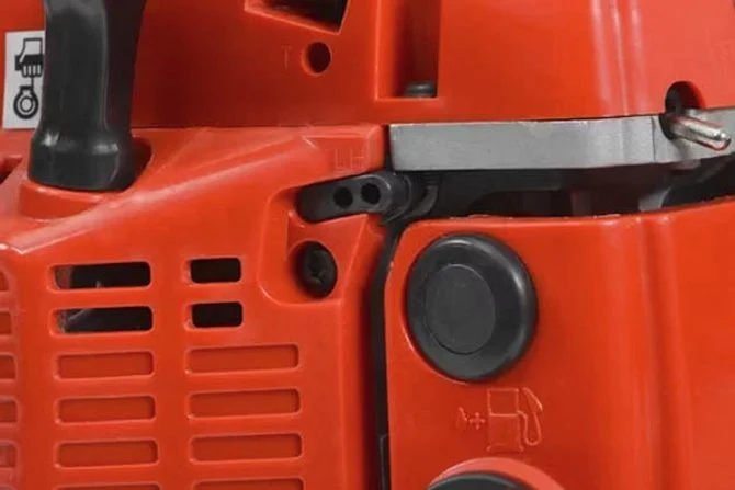 Detail oranžové řetězové pily s viditelnými šrouby pro nastavení karburátoru.