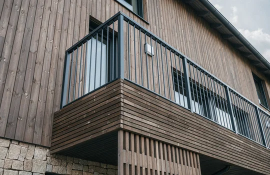 Moderní dřevěný balkon na fasádě domu s impregnovaným obkladem.