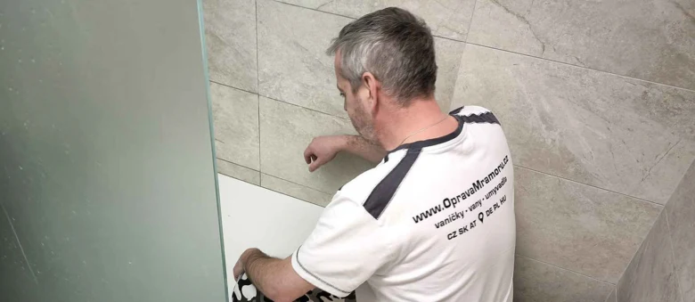 Muž opravuje sprchovou vaničku v koupelně s dlažbou.