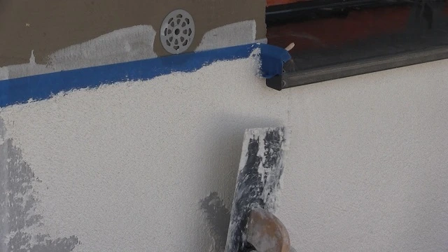 Ruční nanášení bílé omítky na stěnu špachtlí.