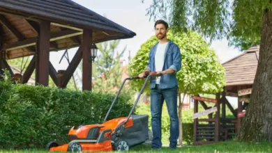 Muž seče trávu oranžovou kosačkou na zelené trávě.
