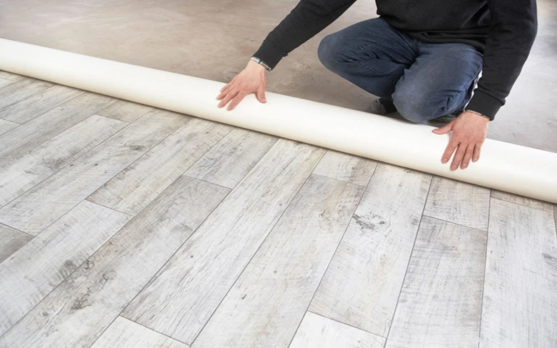Muž rozkládá roli podlahového materiálu na dřevěnou podlahu.