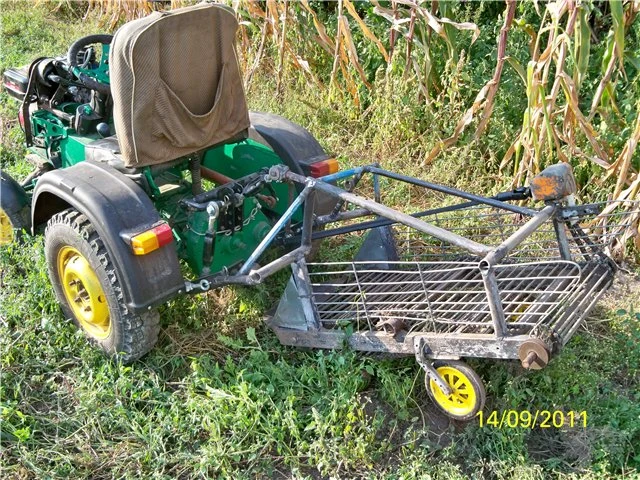 Domácí malý traktor s přívěsem na trávníku u kukuřice.