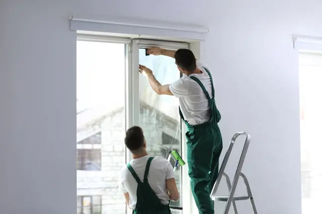 Muži odstraňují starou ochrannou folii z plastového okna.