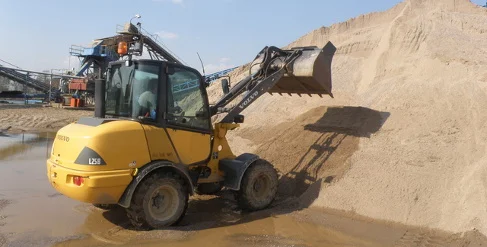 Žlutý nakladač překládá směs písku a štěrku na skladišti.