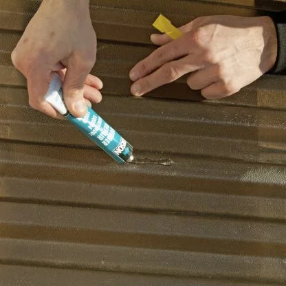 Ruce opravují malou díru v polykarbonátové desce pomocí lepidla.