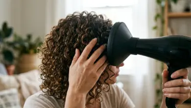 Žena vysušuje kudrnaté vlasy difuzérem na fén.