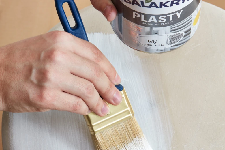 Člověk natírá hladký povrch bílou barvou na plast.