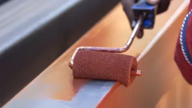 Kovový válec nanáší červenou barvu na pozinkovaný ocelový nosník.