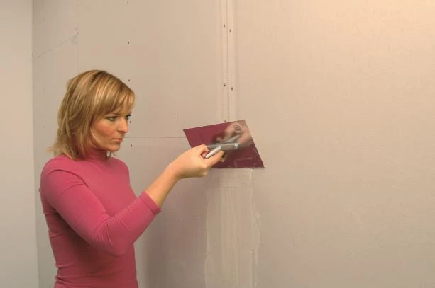 Žena brousí tmel na zdi pro hladký povrch.