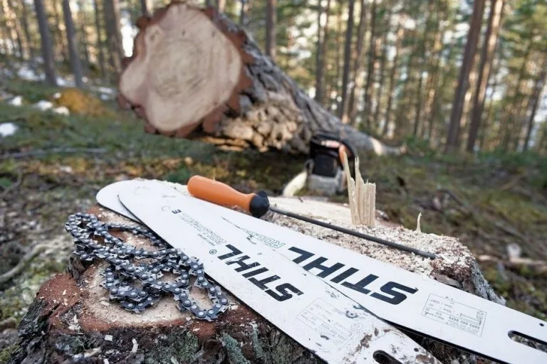 Řetěz motorové pily značky Stihl s označením na liště leží na kmeni stromu v lese.