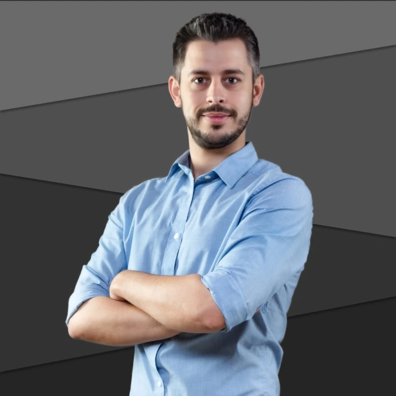 Muž v modré košili stojí s kříženýma rukama.