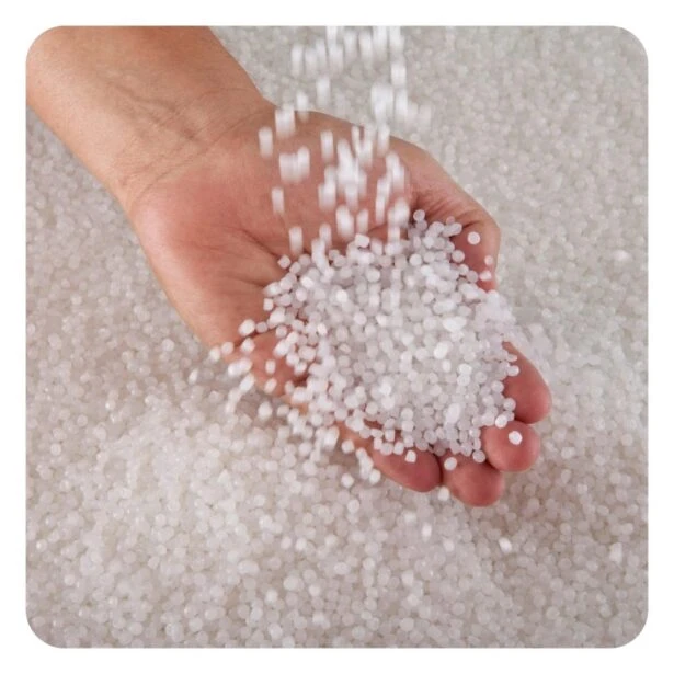 Ruka drží bílé granulované plastové pelety z HDPE.