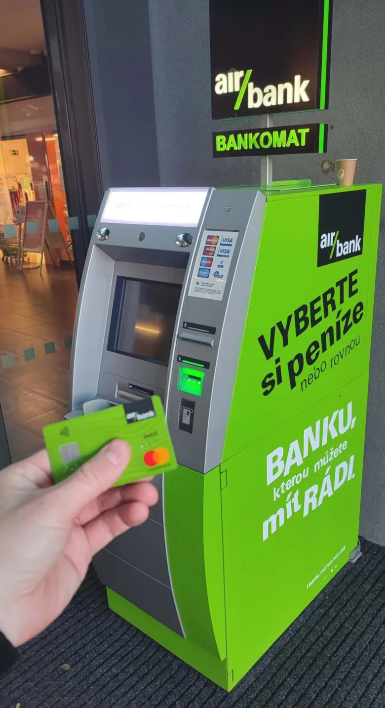 Ruka s kartou před českým bankomatem Air Bank.