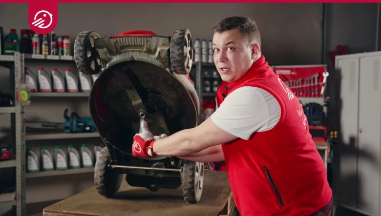 Mechanik opravuje převrácenou sekačku na trávu v dílně.