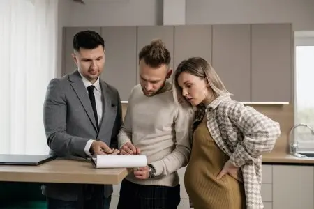 Rodina s realitním makléřem prozkoumává dokumenty v kuchyni.
