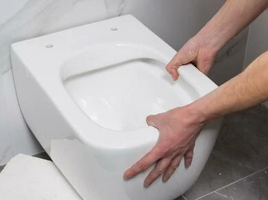 Ruční instalace bílého závěsného WC v koupelně.