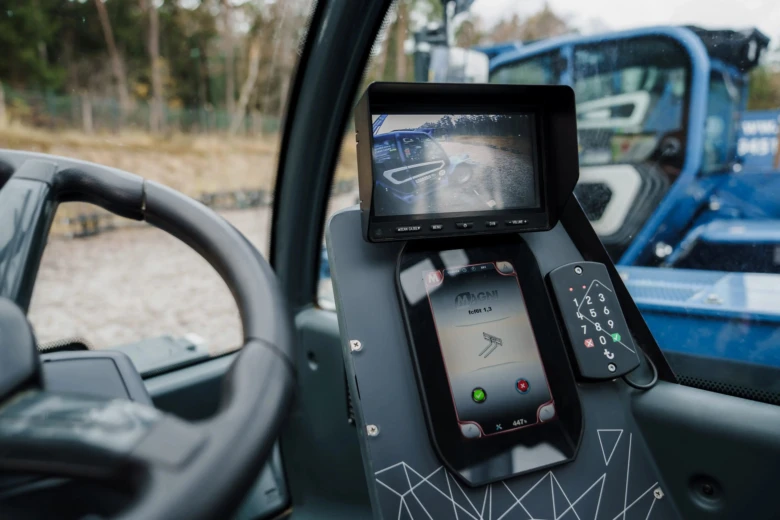 Vnitřek kabiny bagru s digitálními ovládacími prvky a monitory.