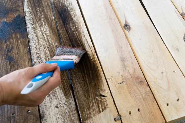 Ruční aplikace impregnace na dřevěné prkno štětcem.