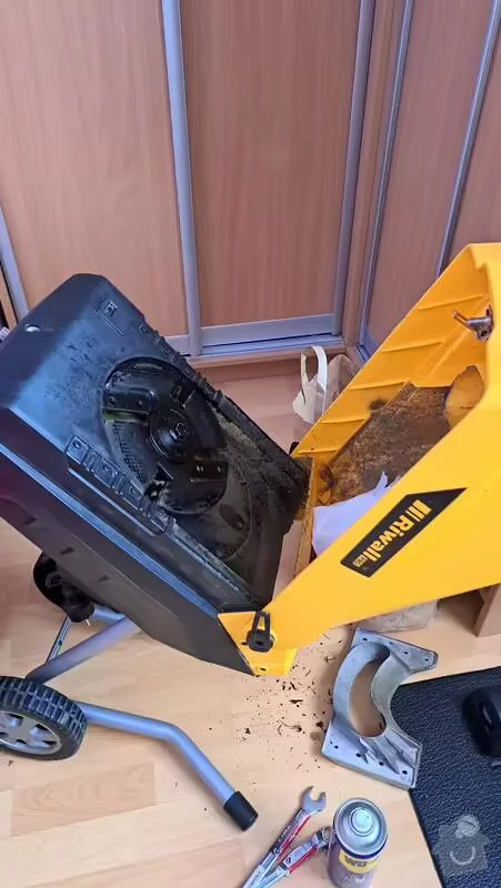 Rozbitá sekačka s odhalenou převodovkou na podlaze.