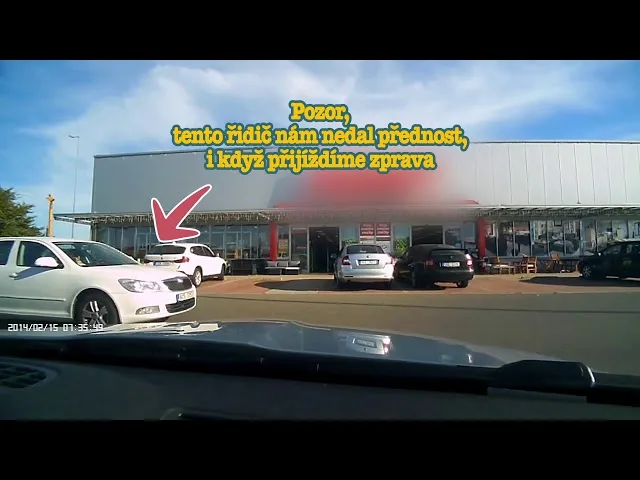 Bílý auto se obrací vpravo na křižovatce před obchodem.