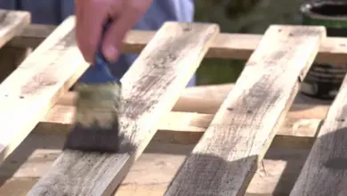 Ruční maření dřevěných paletových prken tmavou barvou.