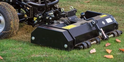 Vertikutátor připevněný k traktoru na trávníku s listím.