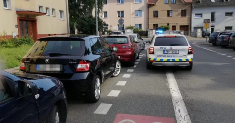Policie u zaparkovaných aut na ulici před domy.