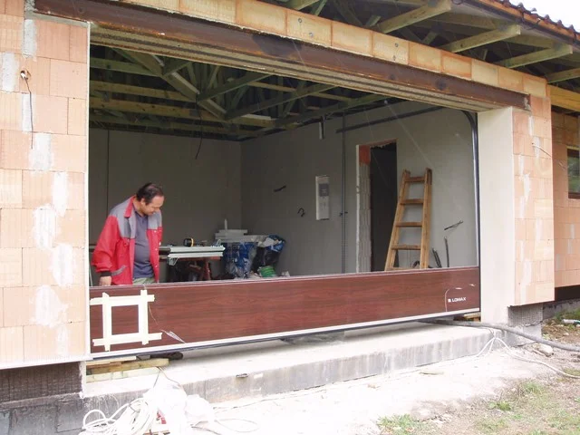 Muž montuje dřevěná garážová vrata v budově.