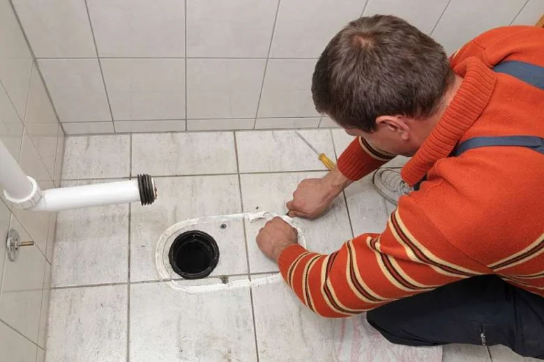 Muž vyměňuje těsnění mezi nádrží a mísou na dlažbě.