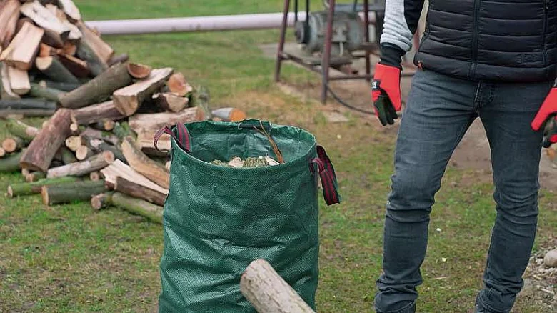 Člověk sbírá ořezané větve do zeleného sáčku na trávníku.