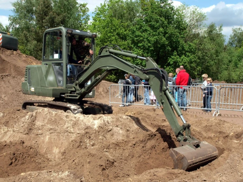 Zelený hydraulický bagr kopá v zemi před divákem.