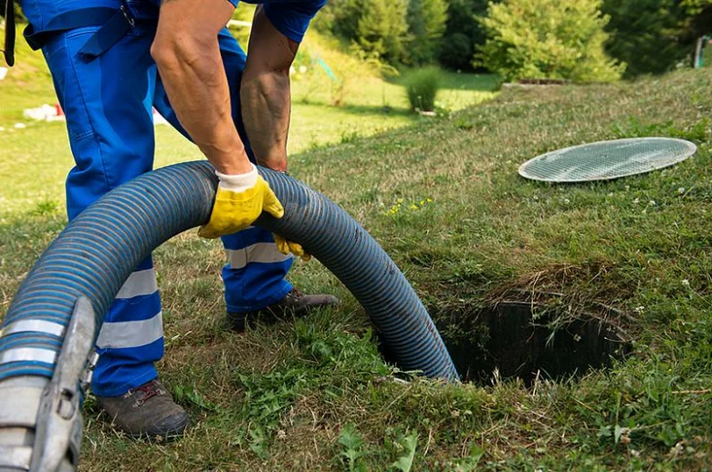 Pracovník opravuje septik na zahradě s otevřeným poklopem.