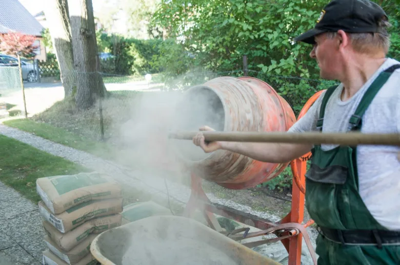 Muž míchá beton v bubnu s pytli cementu vedle.