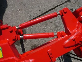 Červené hydraulické válce na rámu taženého pluhu pro nastavení hloubky.