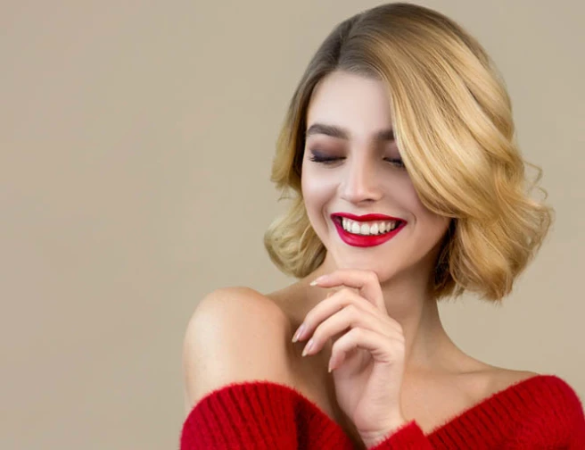 Žena s krátkými vlnitými blond vlasy se širokým úsměvem.