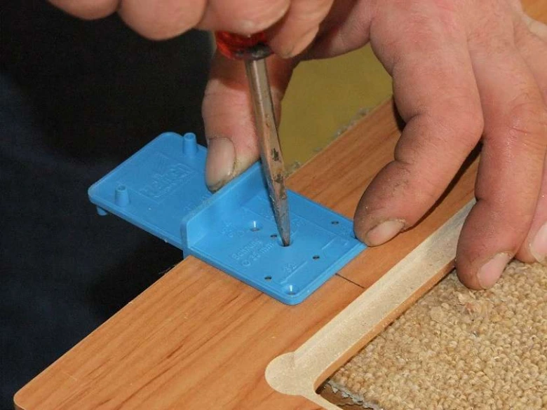Vrtání otvorů pro panty na dřevěném nábytku pomocí modrého vodítkového nástroje.
