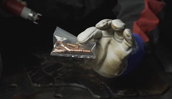 Ruka v rukavici drží sáček s měděnými elektrodami pro řezání plazmou.